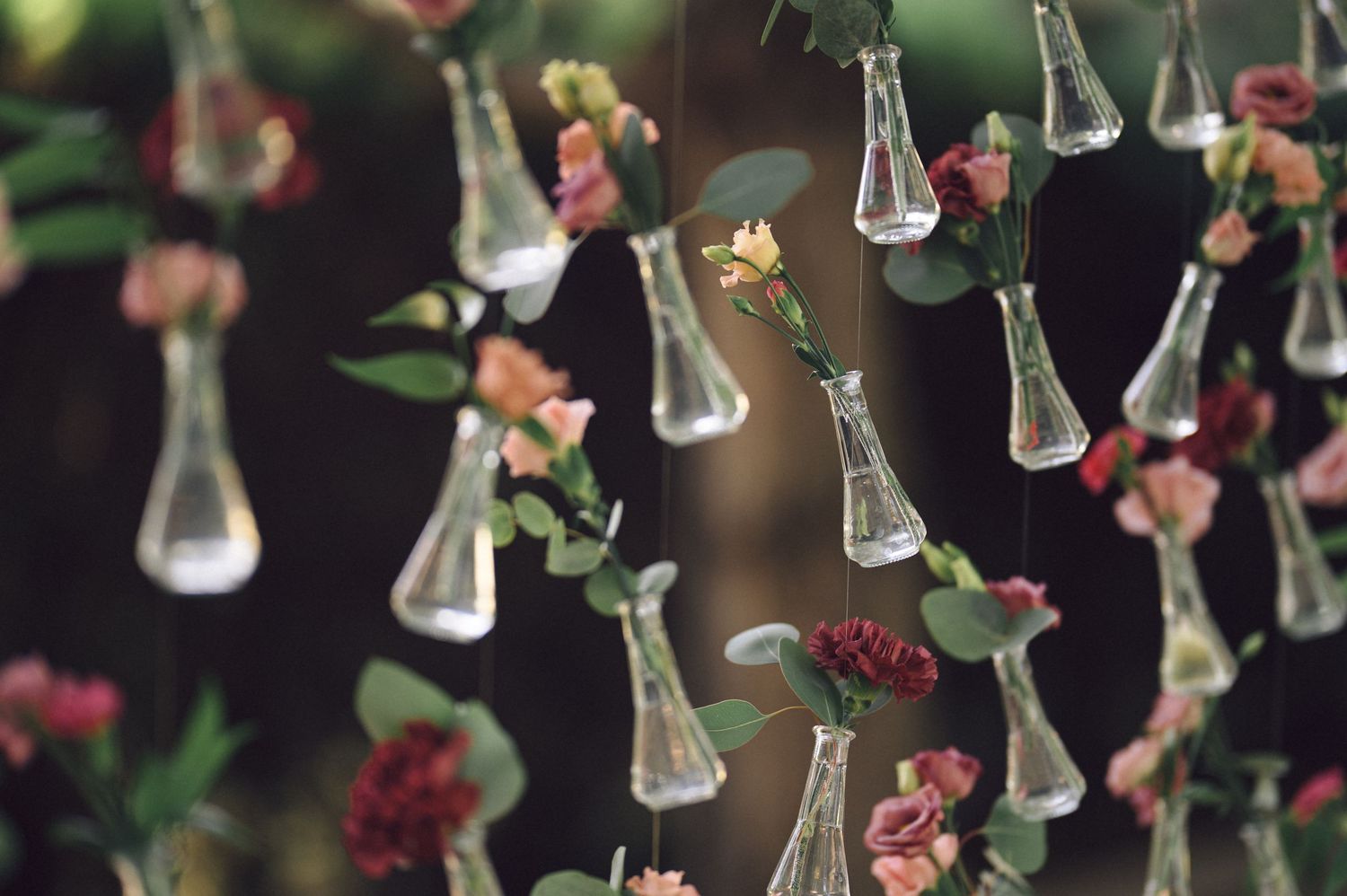Hanging glass vases with delicate pink and green floral stems create an ethereal ceiling display.