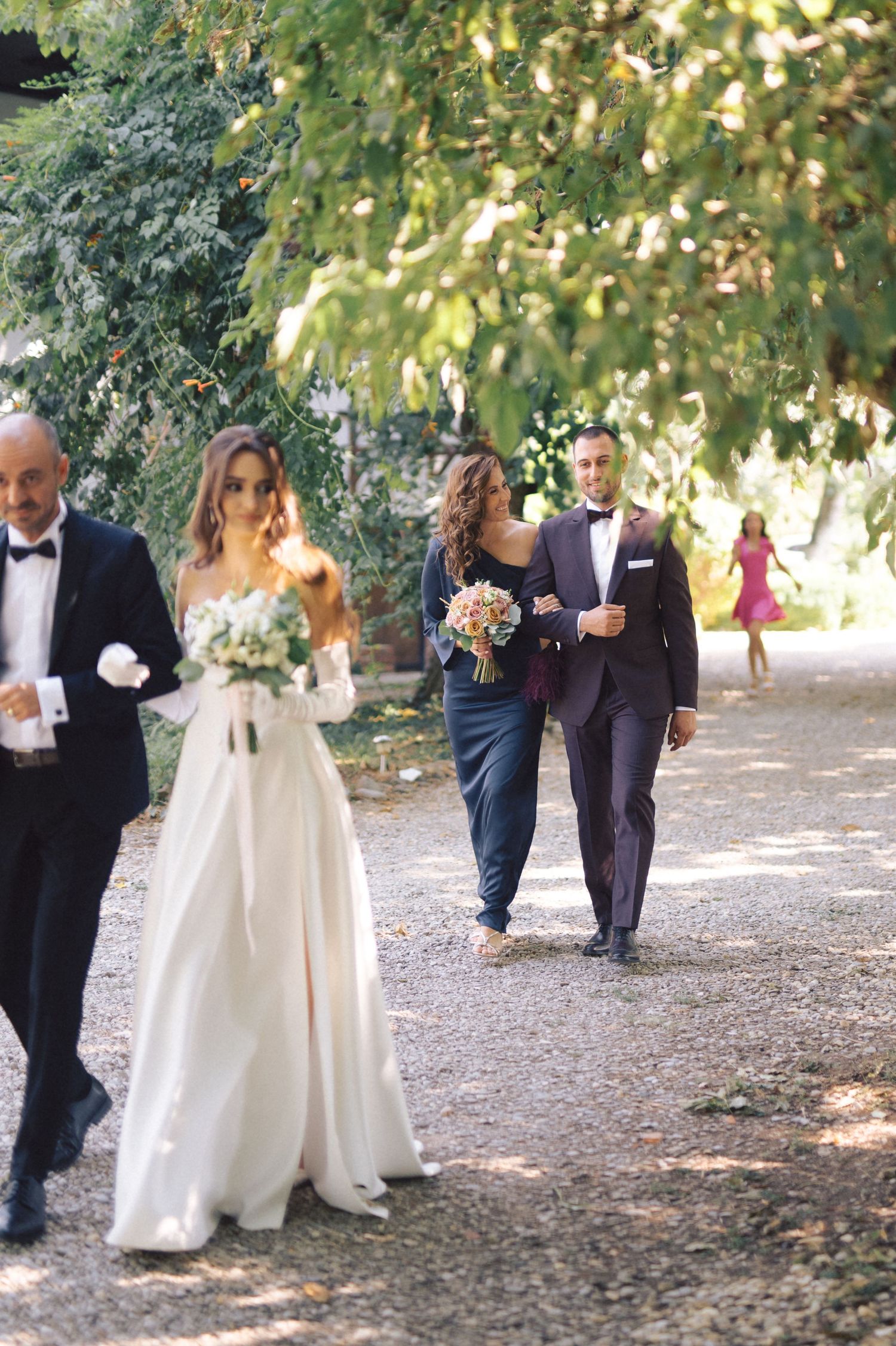 Wedding party and guests walk along a tree-lined path in a casual progression across five candid photos.