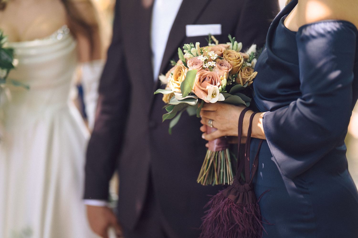 Newlywed couple holds elegant wedding bouquets while wearing traditional white dress and navy suit at outdoor ceremony.