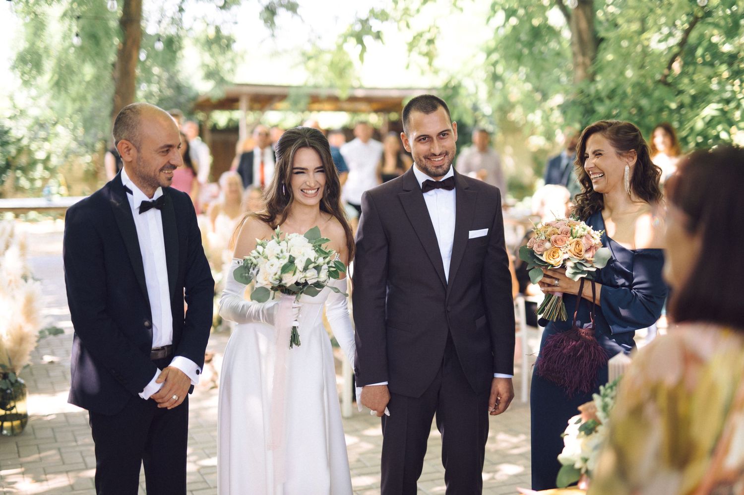 Outdoor wedding celebration showing guests enjoying a candid moment among trees with natural lighting.