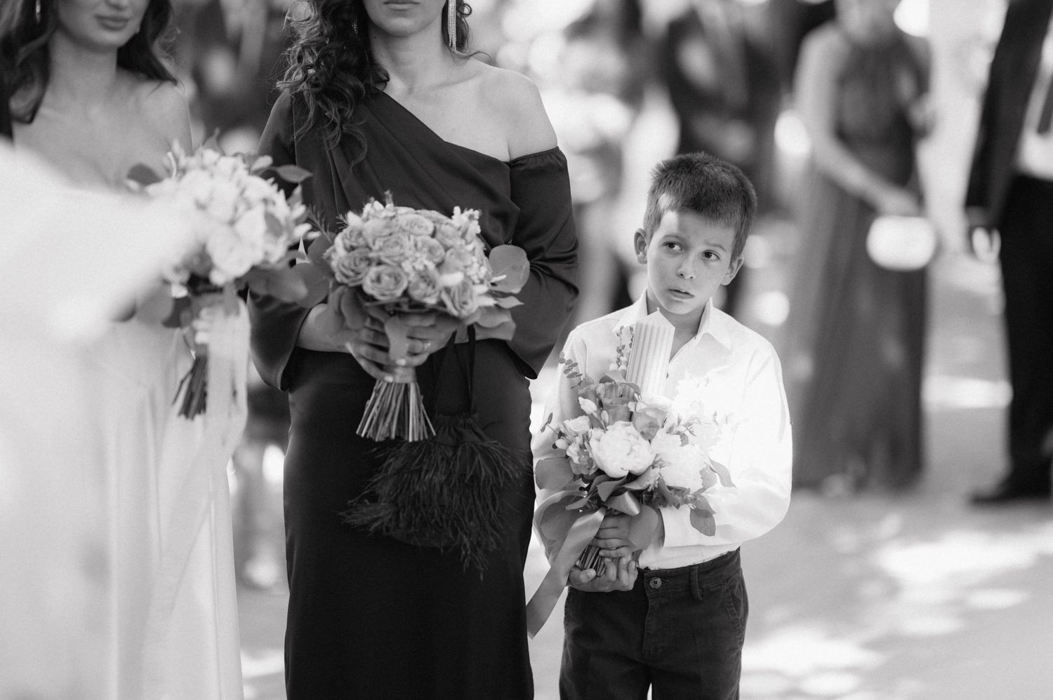 A wedding party group poses outdoors with elegant bouquets and formal attire.