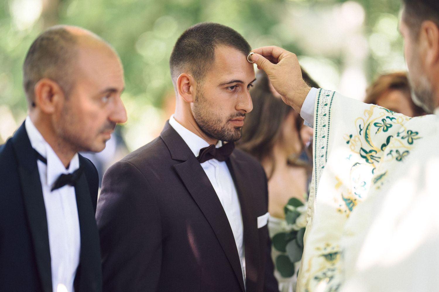 A row of formally dressed guests in black suits and dresses mingle outside at an elegant wedding reception.