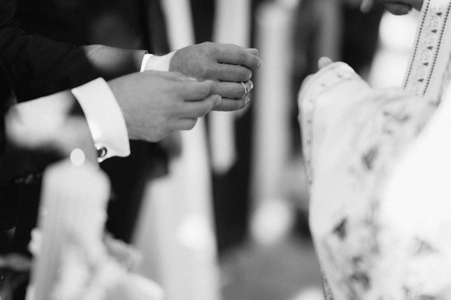 Black and white close-up shot of hands exchanging wedding rings during a marriage ceremony.