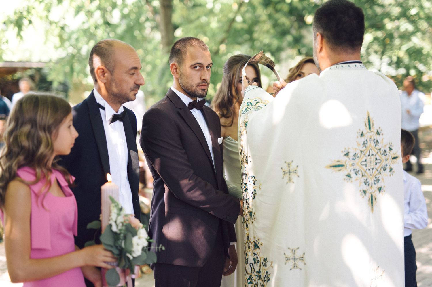 People gather at an outdoor wedding reception under white floral decor and trees.