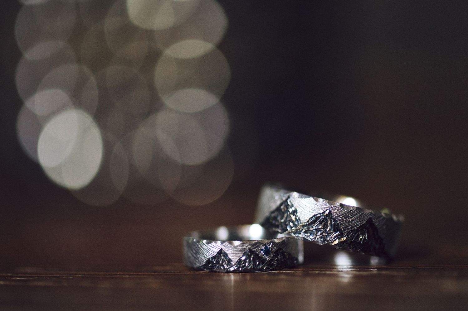 Wedding rings with diamonds sparkle against a dark background with soft bokeh lights.