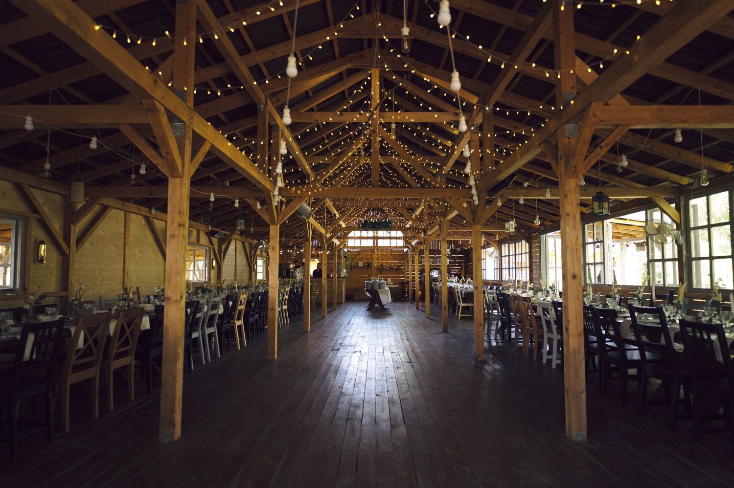 Rustic barn interior decorated with string lights features exposed wooden beams and an expansive open floor plan for events.