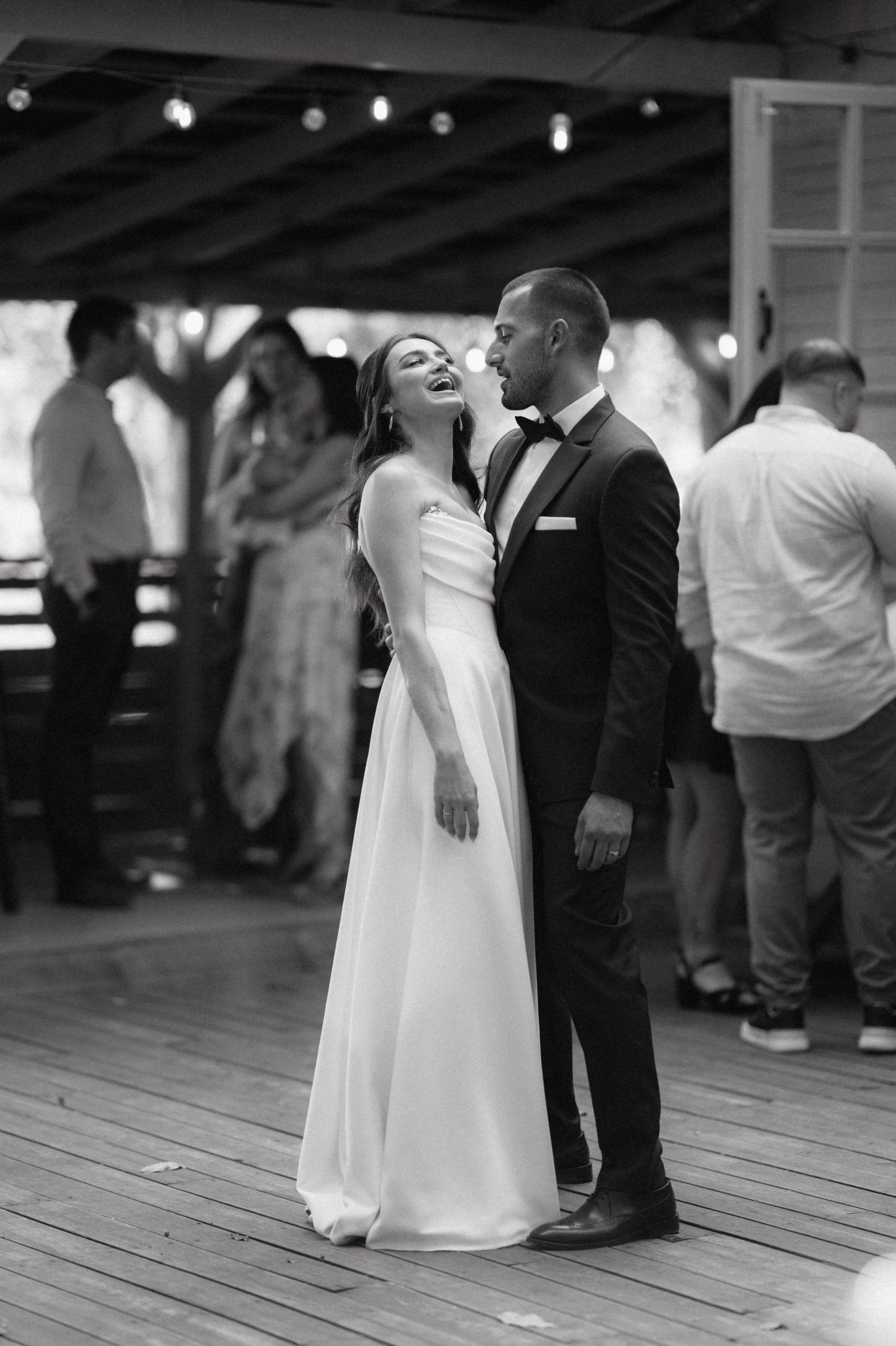 A bride and groom share a romantic first dance on a wooden floor at their wedding reception.
