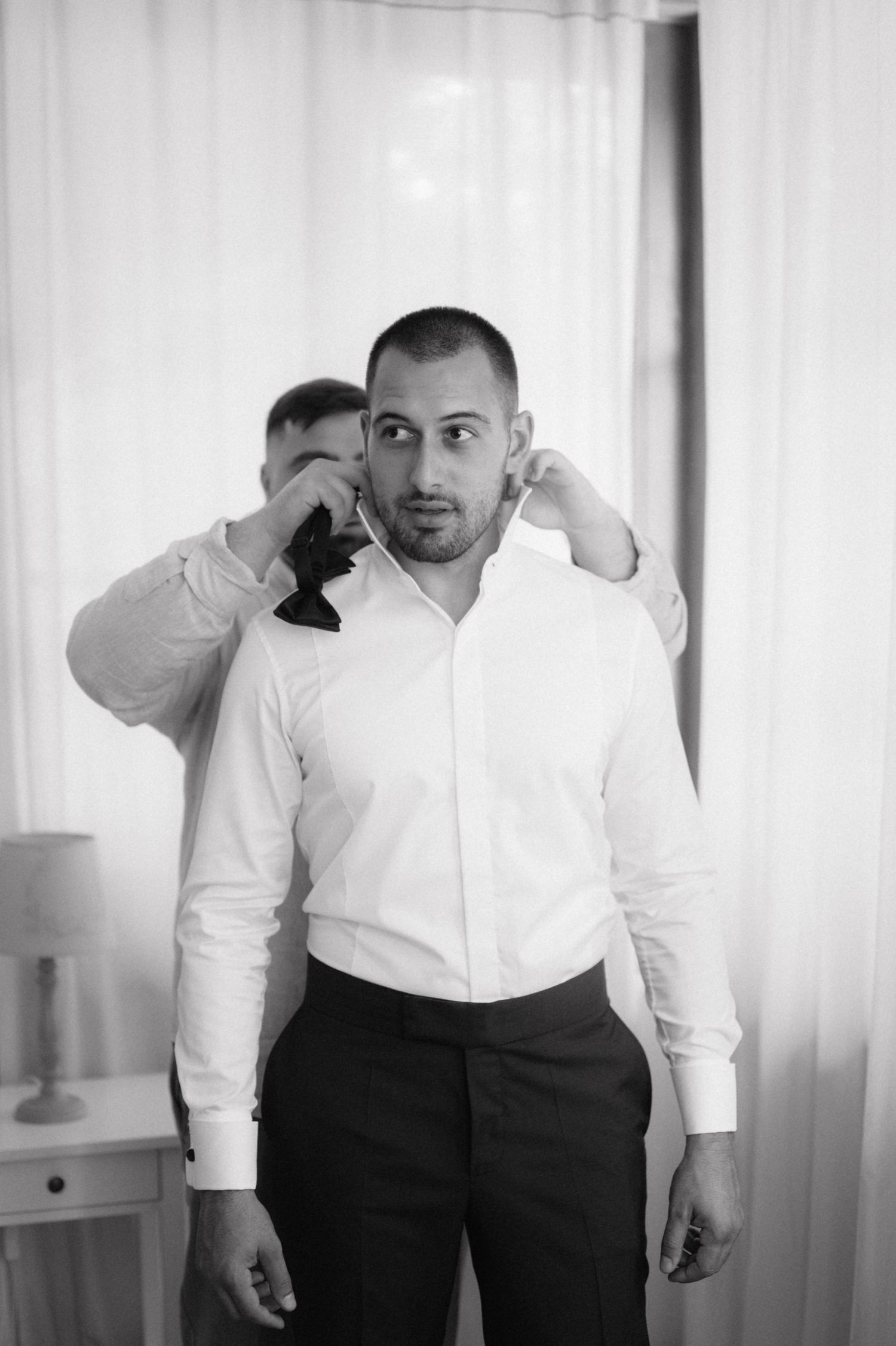 A series of photos showing a person in a white dress shirt and black pants adjusting their bowtie in a bright room.