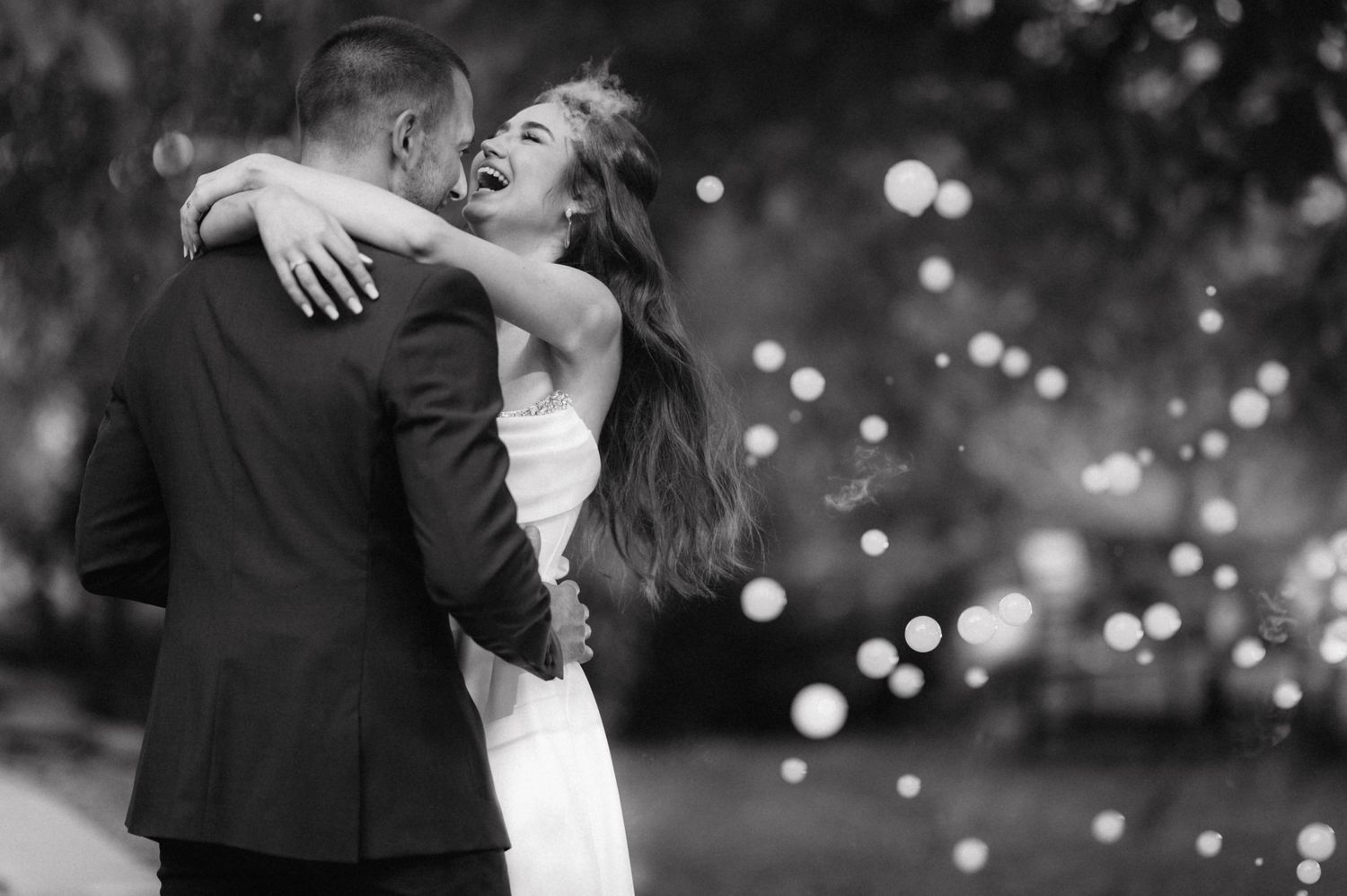 Silhouettes of happy couple dancing together at a wedding celebration with glowing bokeh lights in the background.