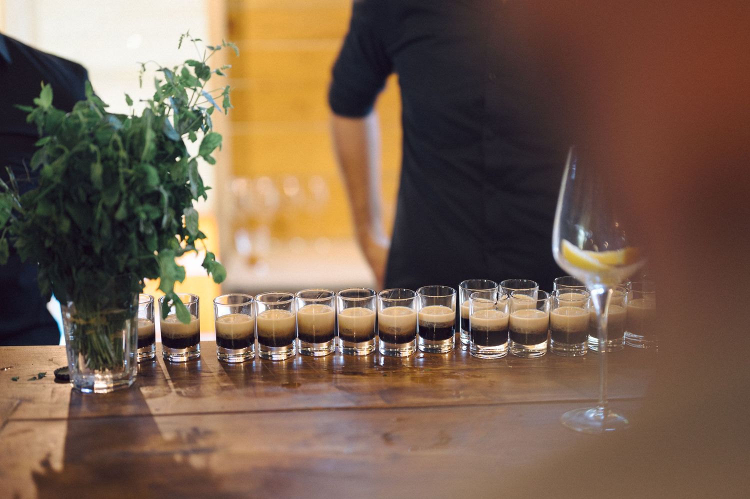 A row of glass tasting cups lined up on a wooden table with warm lighting in the background.