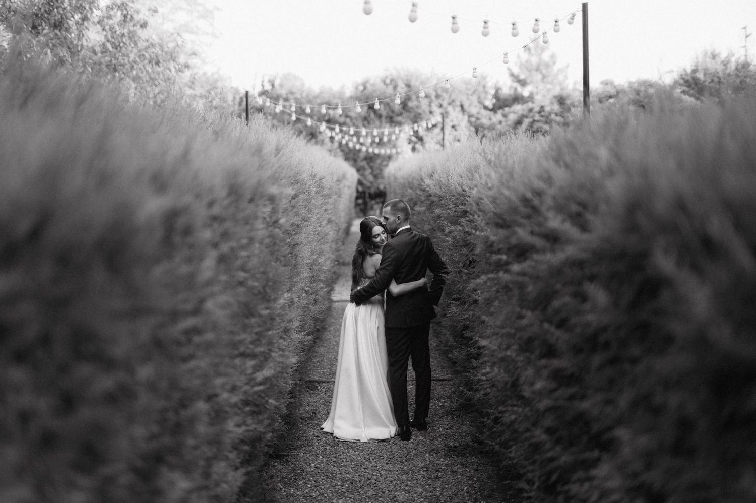 Black and white romantic silhouette of couple walking through a landscaped garden pathway.