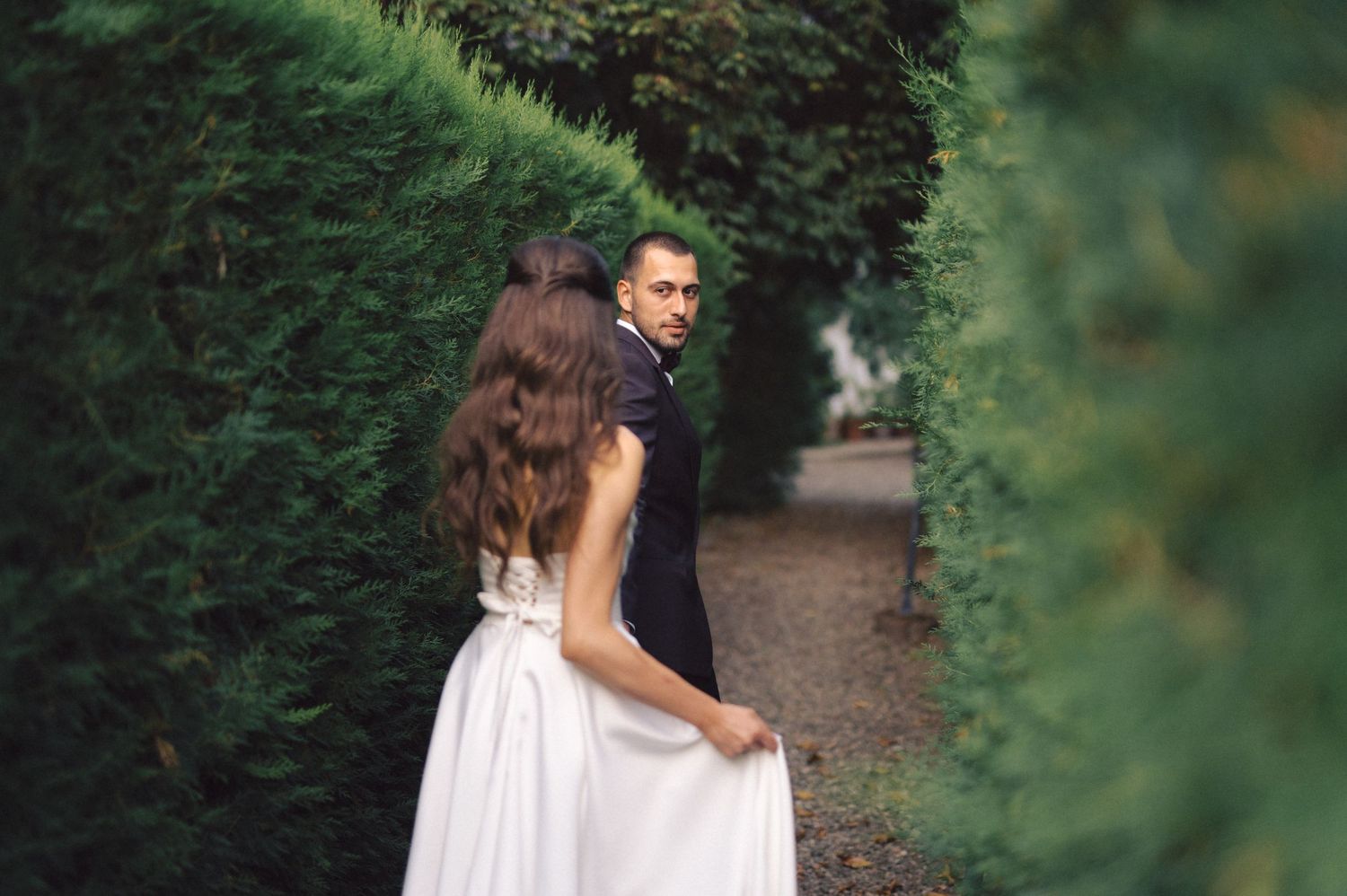 Couple walks through lush garden pathway surrounded by greenery.