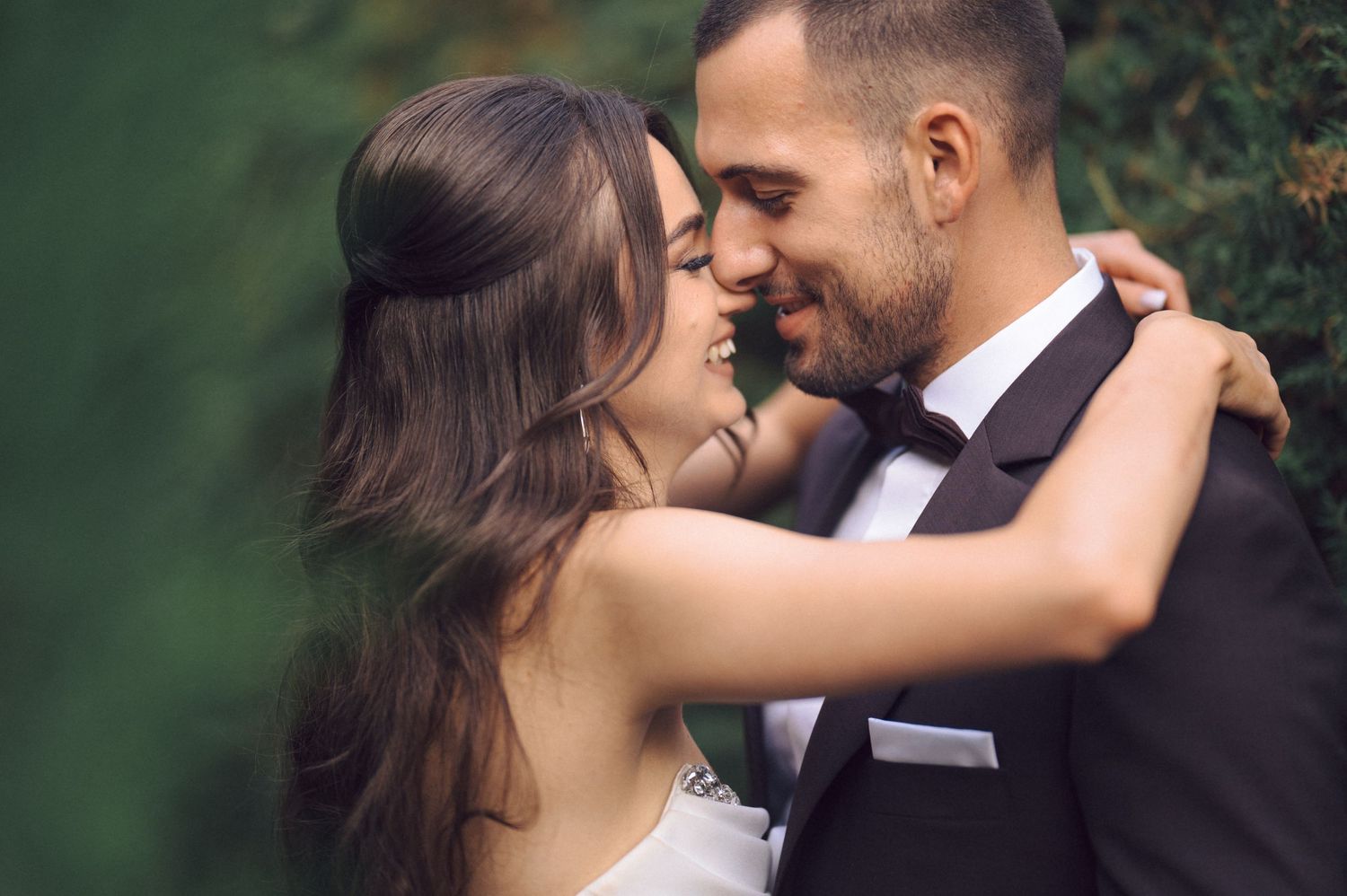 Romantic outdoor wedding portrait of couple embracing in garden setting.