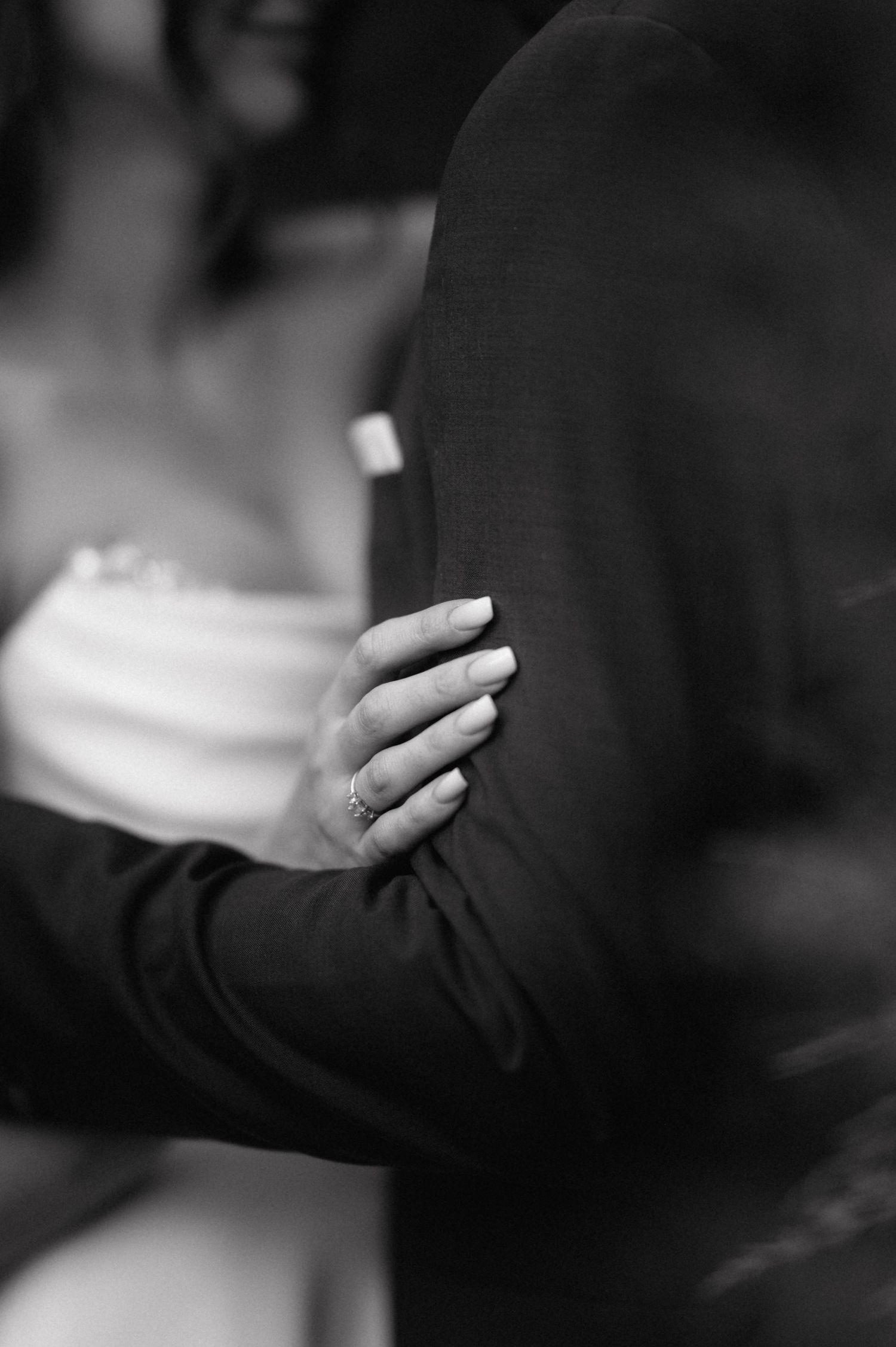 Black and white close-up of hands with engagement ring holding each other in an intimate embrace.