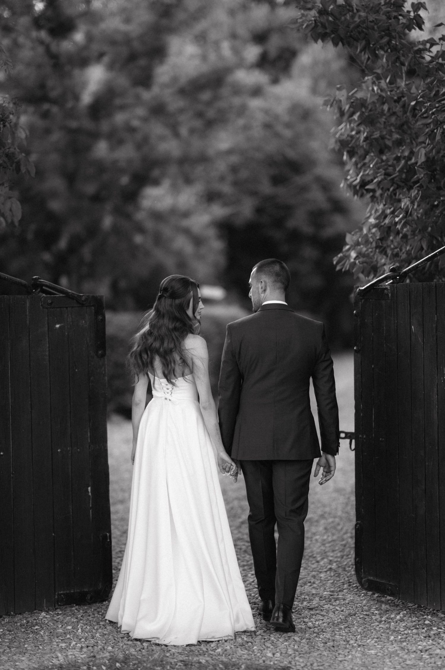 Black and white sequence of newlyweds walking down a garden path in their wedding attire, captured from behind.