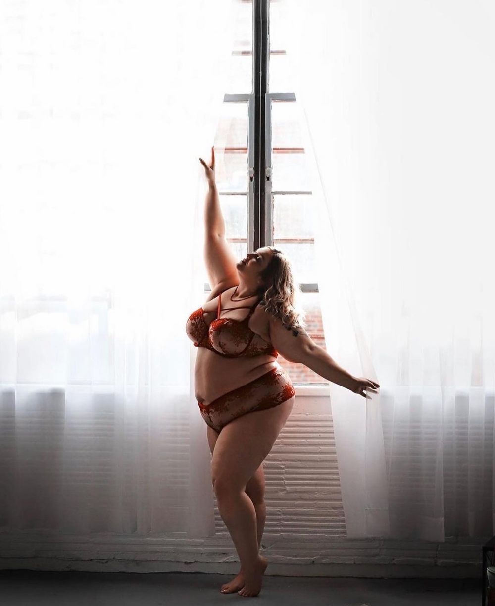 Plus size Silhouette dancing against window light in artistic boudoir photography.