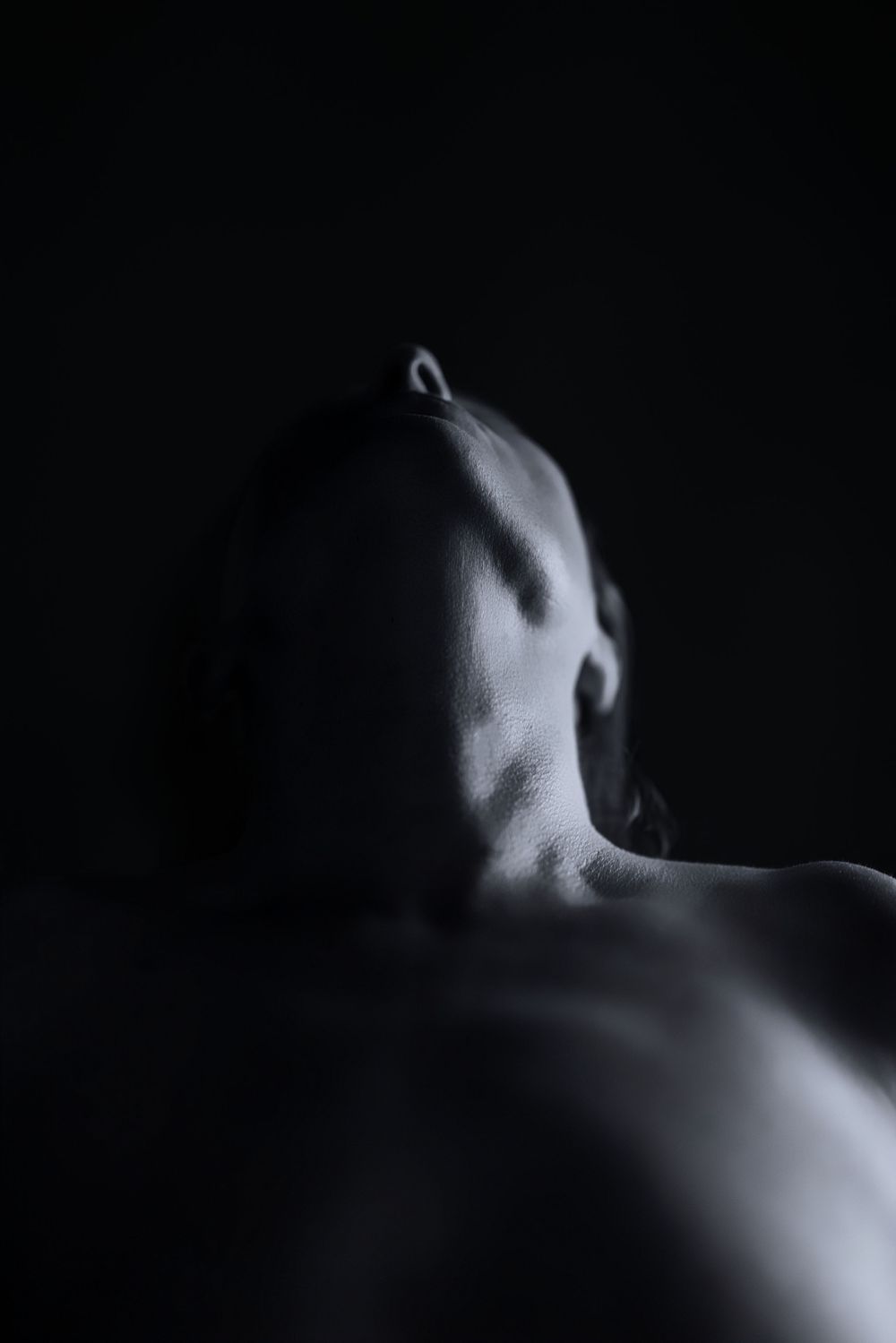 Dramatic black and white fine art photograph of a bald human figure with head tilted back against dark background.