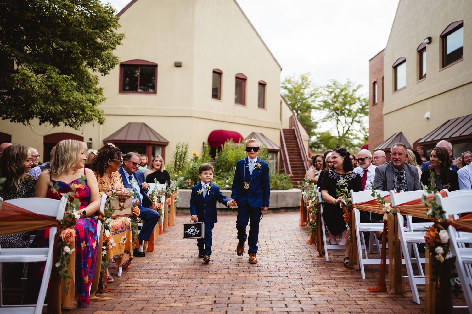 Wedding guests walk along a brick-paved pathway at an elegant outdoor venue during a daytime celebration.