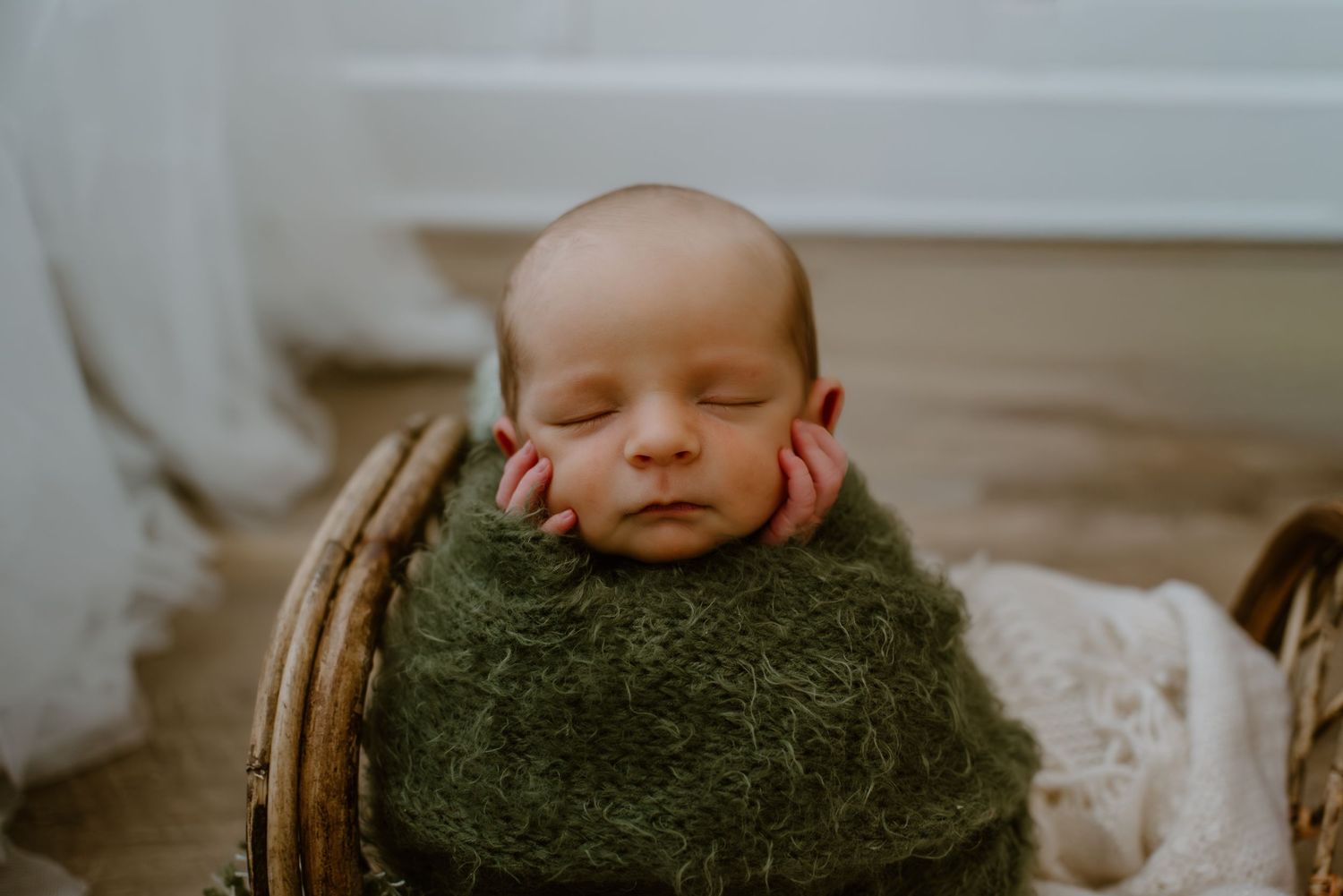 Sleeping newborn baby wrapped in green knit blanket during professional photo session.