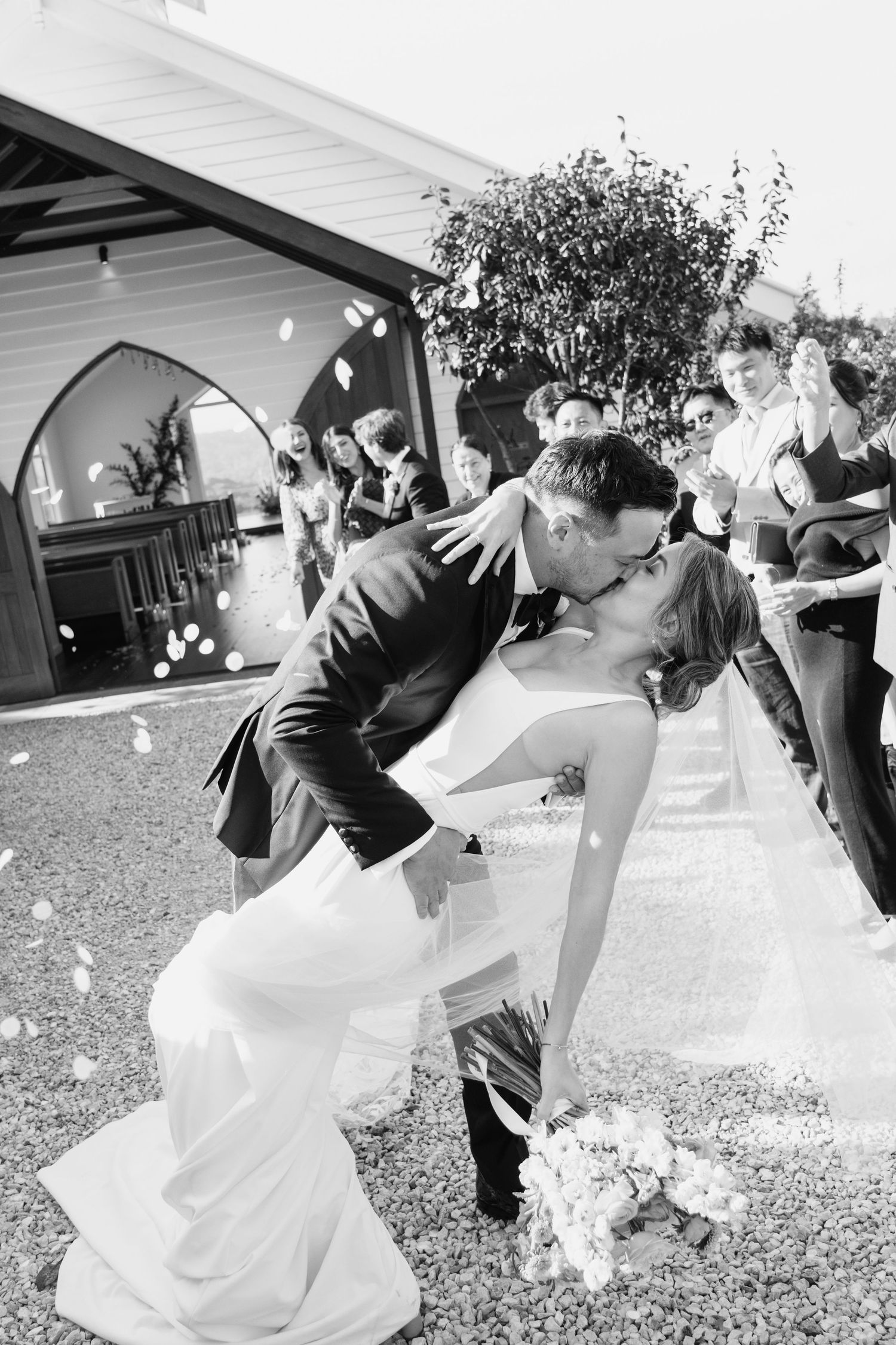 A series of black and white photos showing a joyful wedding celebration with dancing and confetti on a sunny outdoor lawn.