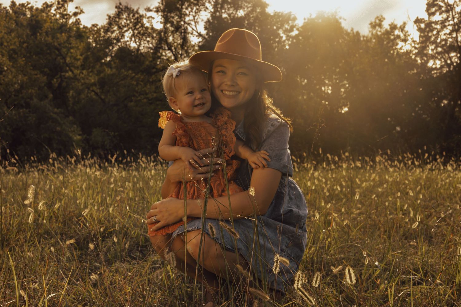 Family photoshoot in golden sunlit field with wildflowers at sunset.