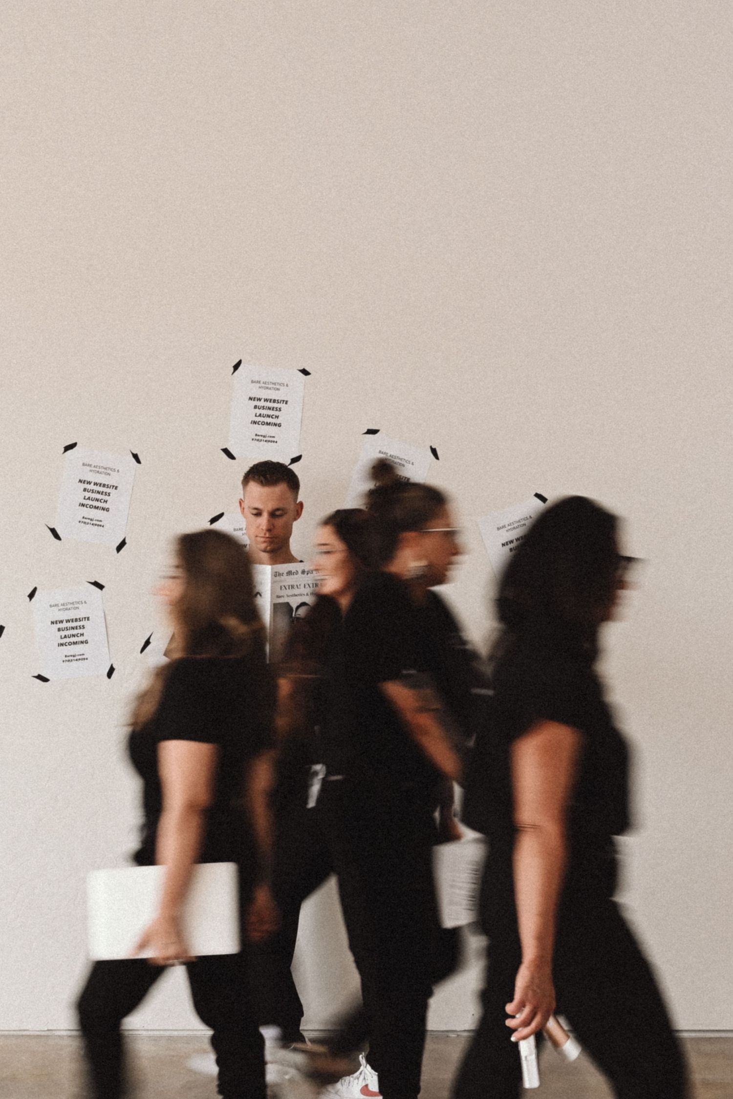 Motion blur captures group walking past white wall with papers in artistic black and white shot.