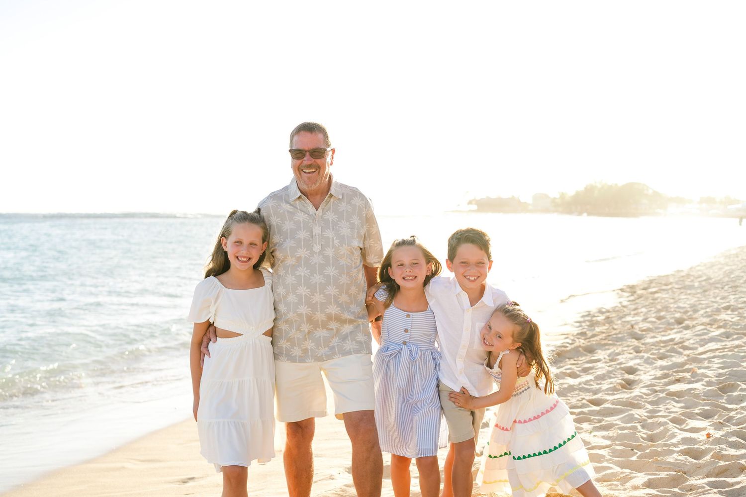 People walking together on a sandy beach at sunset in coordinated white and light blue outfits. Oahu family photography, Hawaii family photo