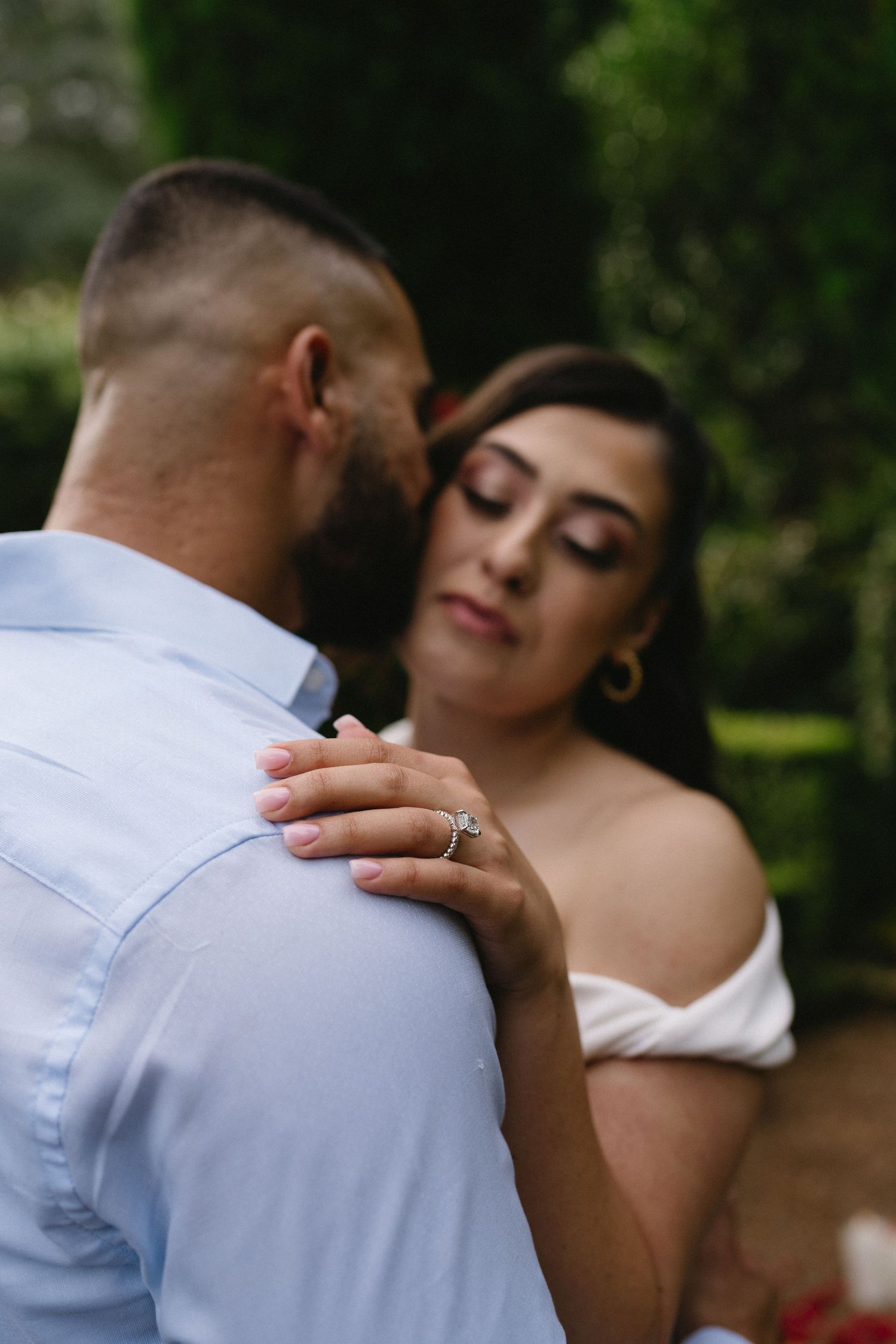 A tender moment between a couple in formal attire against a backdrop of greenery.