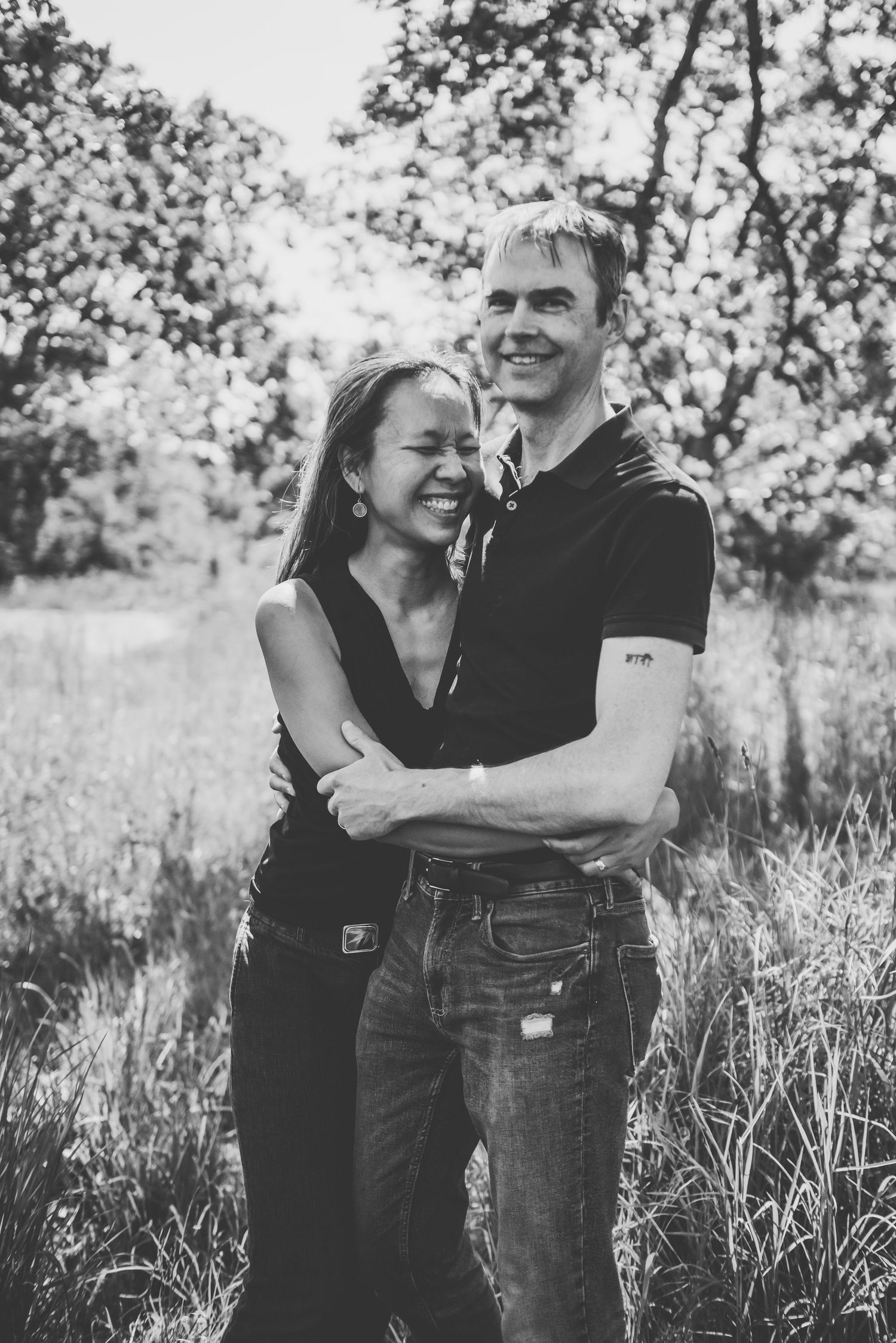 Happy couple embracing and laughing together in a sunlit, overgrown grassy field.