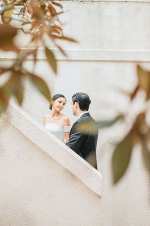 A romantic wedding moment framed by leaves as couple stands on white staircase.
