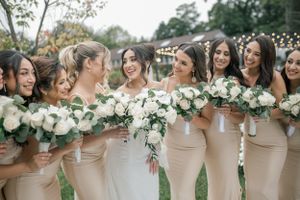 Bridesmaids in champagne-colored dresses hold elegant white bouquets while sharing a candid moment outdoors.