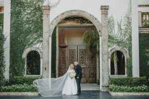 Elegant couple stands before grand arched at Bell tower in Houston, TX  wooden doors and ivy-covered walls at historic venue.