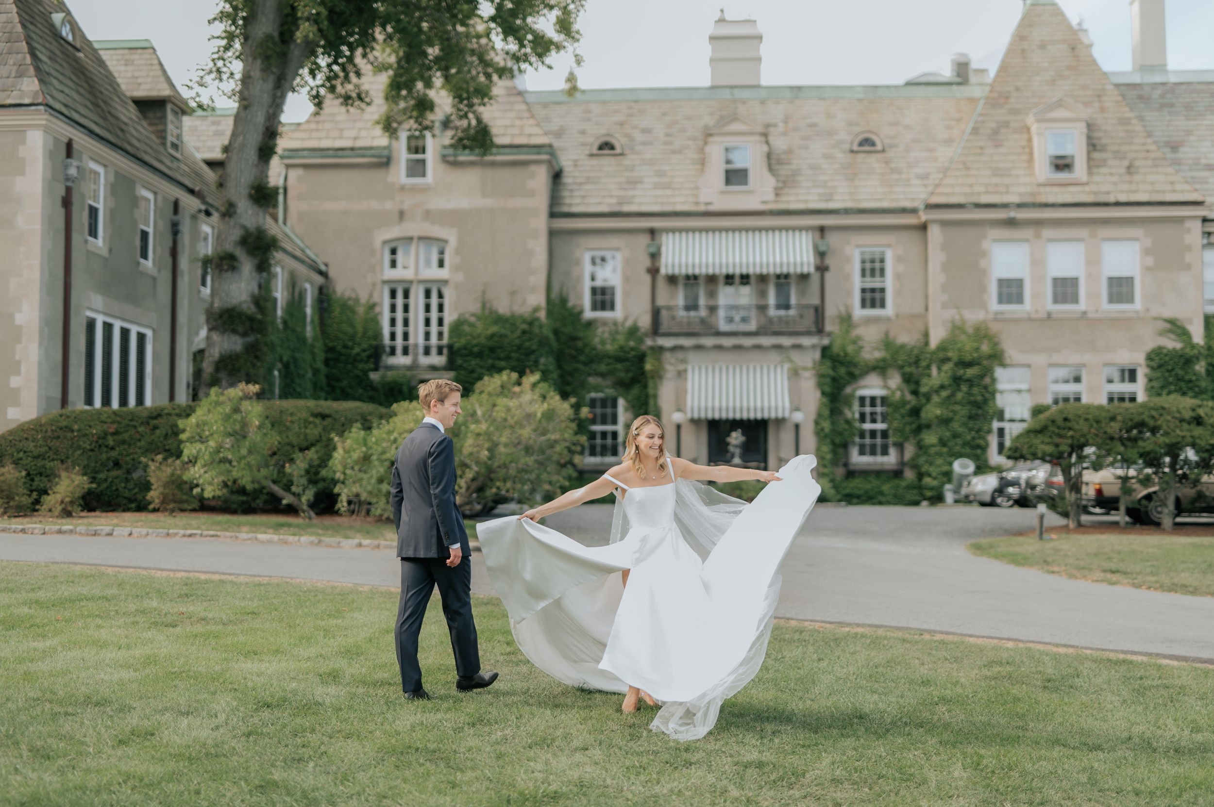 A couple dances together on a manicured lawn in front of New York yacht club in Newport, RI mansion on their wedding day.