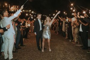 Wedding guests create a sparkler tunnel exit for the couple celebrating in a silver sequined dress at night.