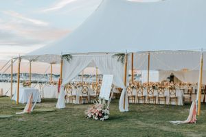 Elegant outdoor wedding reception in Newport setup with white draped canopies and tables on a grassy lawn overlooking the water at sunset.