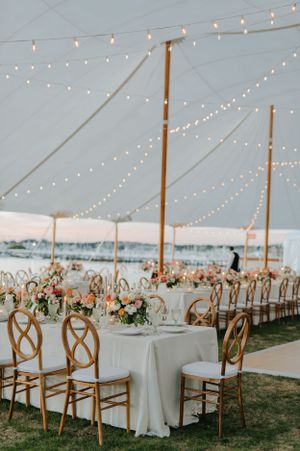 Elegant outdoor wedding reception in Newport, RI setup with string lights, wooden crossback chairs and white tablecloths under a tent.