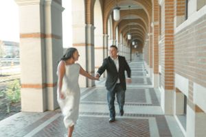 A couple runs playfully through an elegant arched corridor in formal wedding attire.