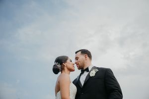 Intimate wedding portrait against cloudy sky with dramatic lighting.