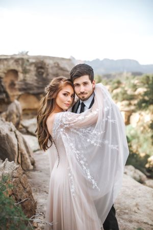 A dreamy wedding portrait showing couple embracing against rocky desert landscape.