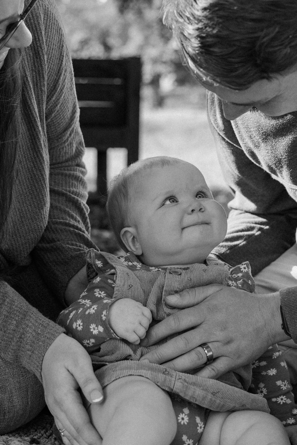 A heartwarming black and white photograph of a baby sharing a special moment with her parents while wearing floral clothing.
