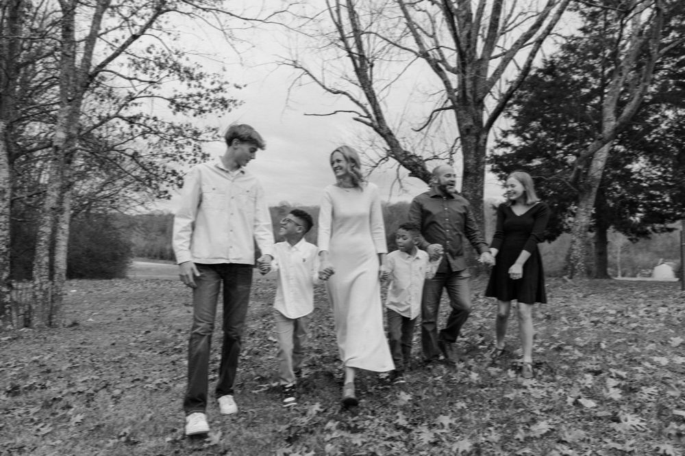 A family of five people walk together outdoors in a black and white photo with bare trees in the background.