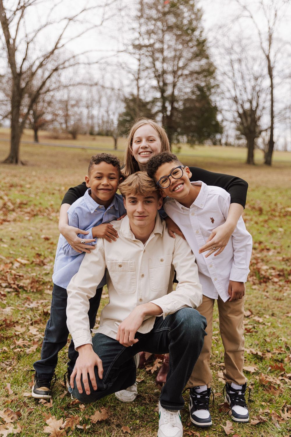 Siblings pose playfully together during a fall photo session outdoors with autumn leaves on the ground.