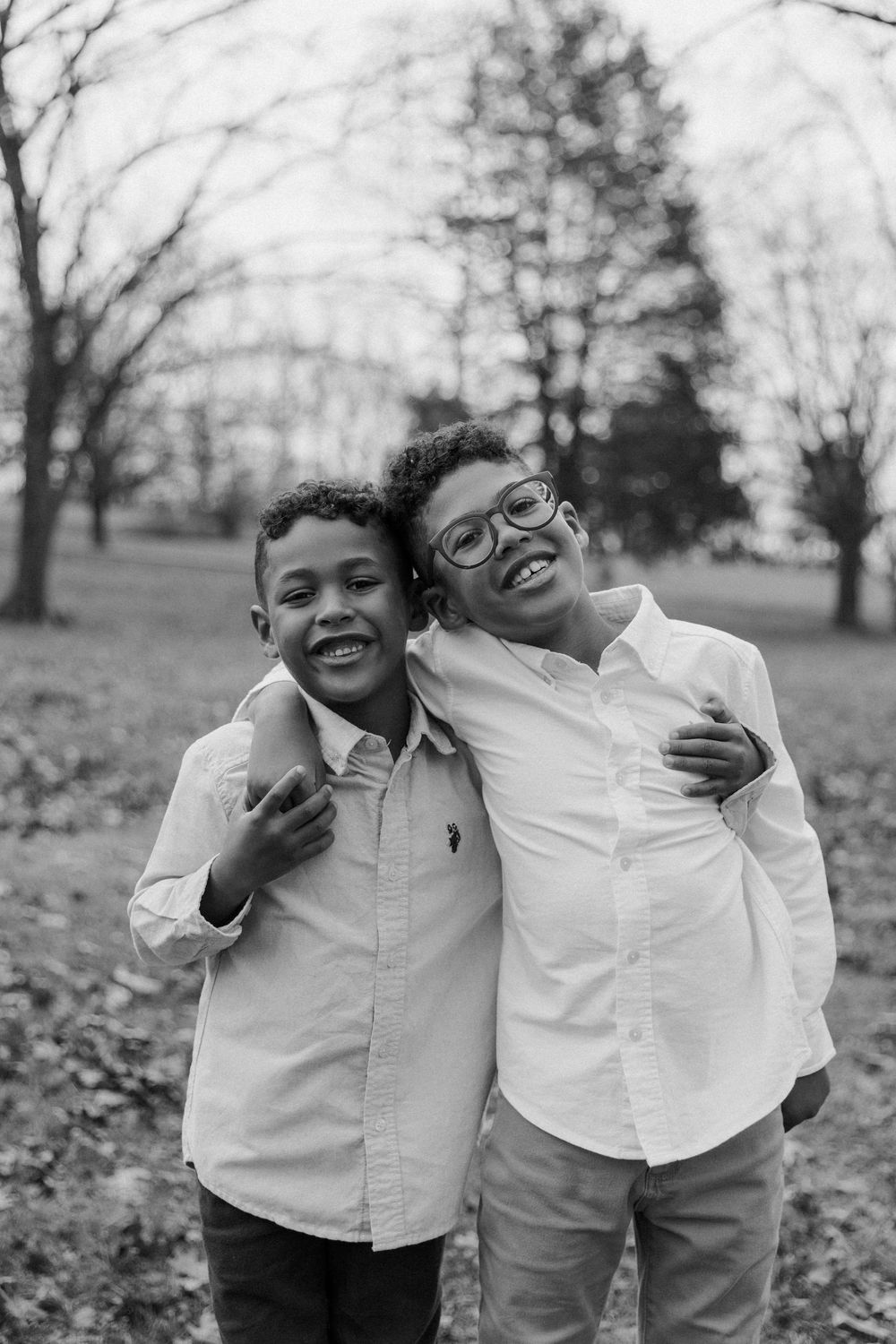 Black and white portrait of two young siblings in white shirts smiling and embracing outdoors in autumn.