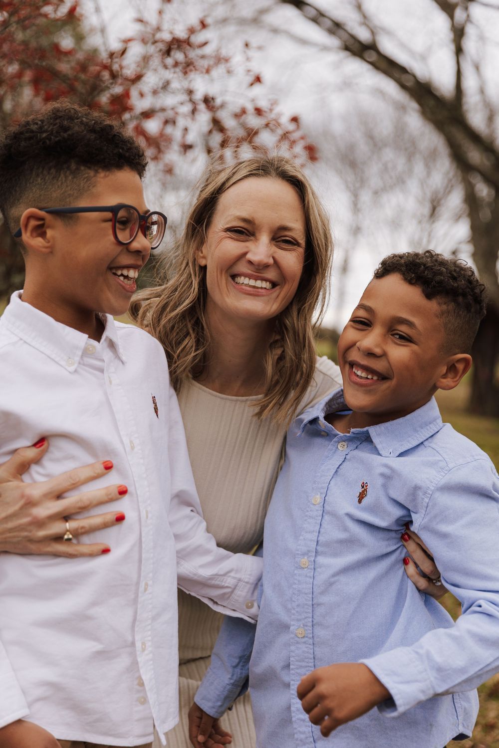 A joyful family moment outdoors with two kids in button-down shirts and a woman in a beige sweater sharing smiles together.