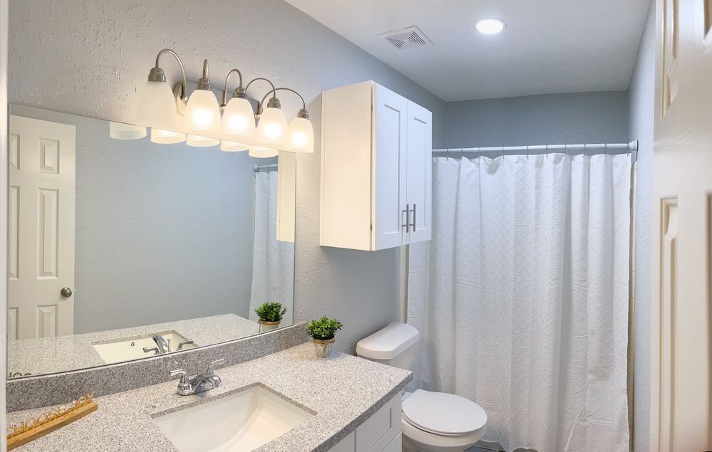 Modern bathroom interior with white cabinets, mirror, and contemporary lighting fixtures.