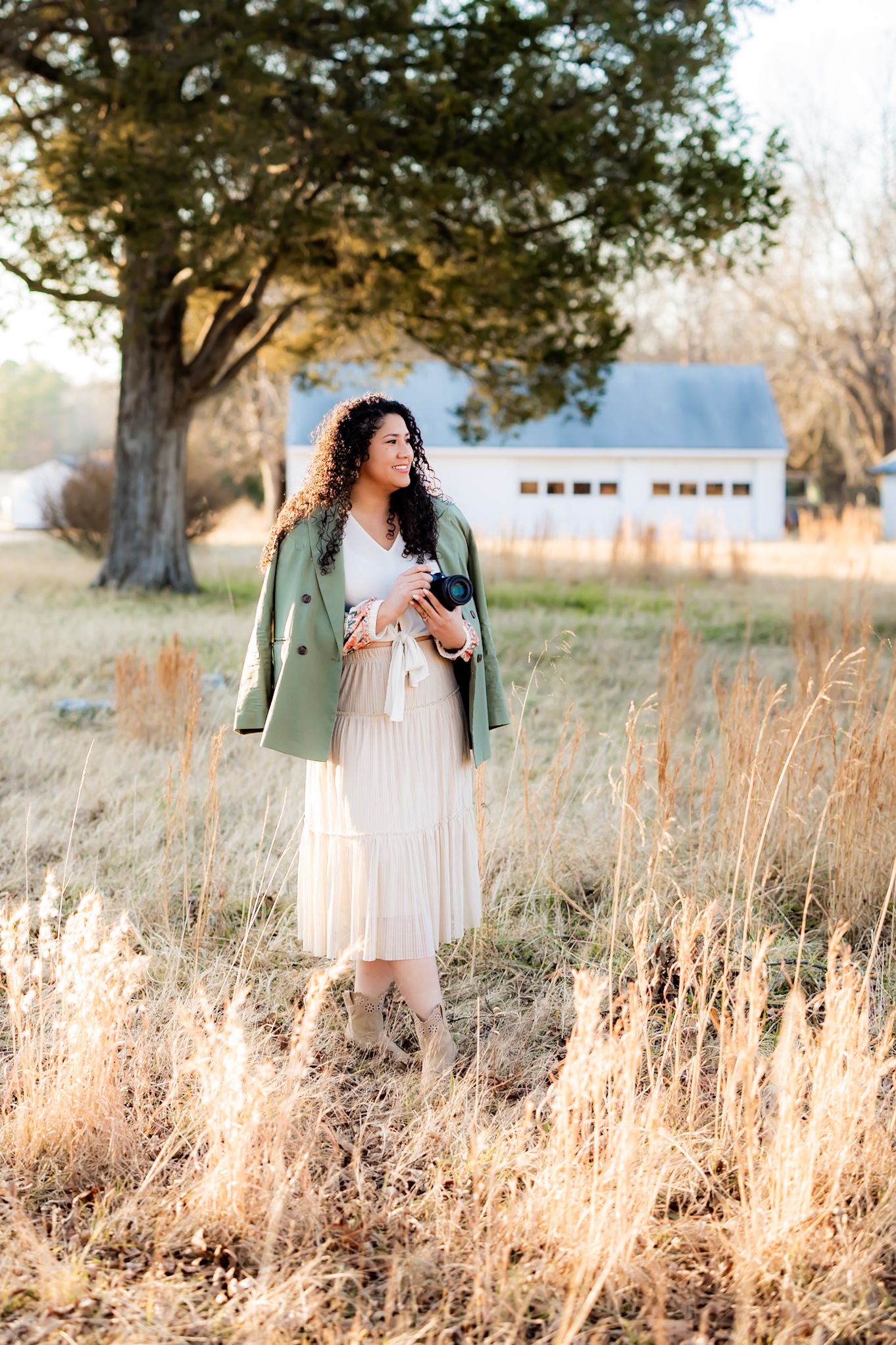 Woman in white dress standing in golden field during sunset with trees in background. RVA Senior graduation photographer. Richmond VA