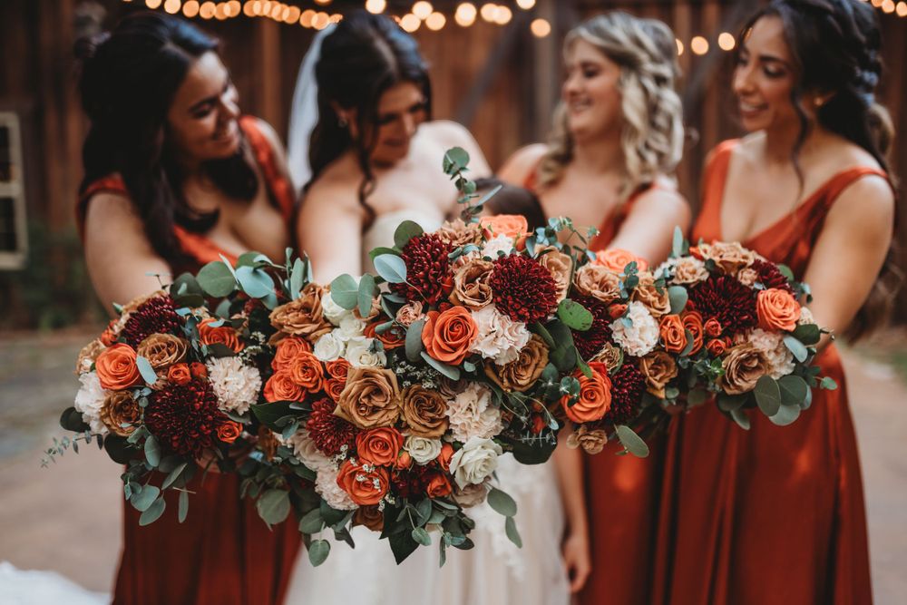 Close-up of wedding bouquets featuring coral roses and mixed flowers held by bridesmaids in rust-colored dresses.