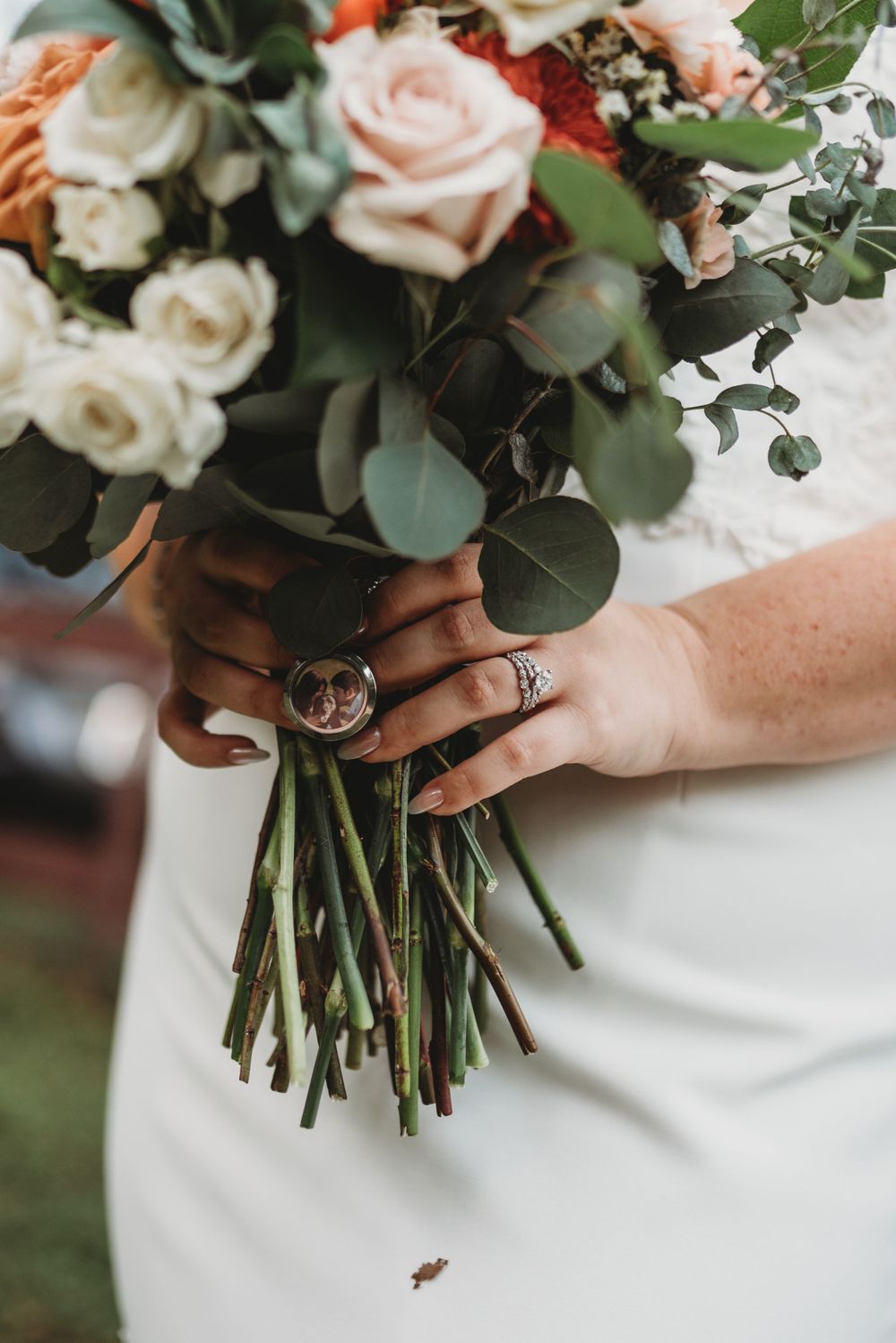 Detail shot of hands holding wedding bouquet with pink roses and eucalyptus, showing engagement ring.