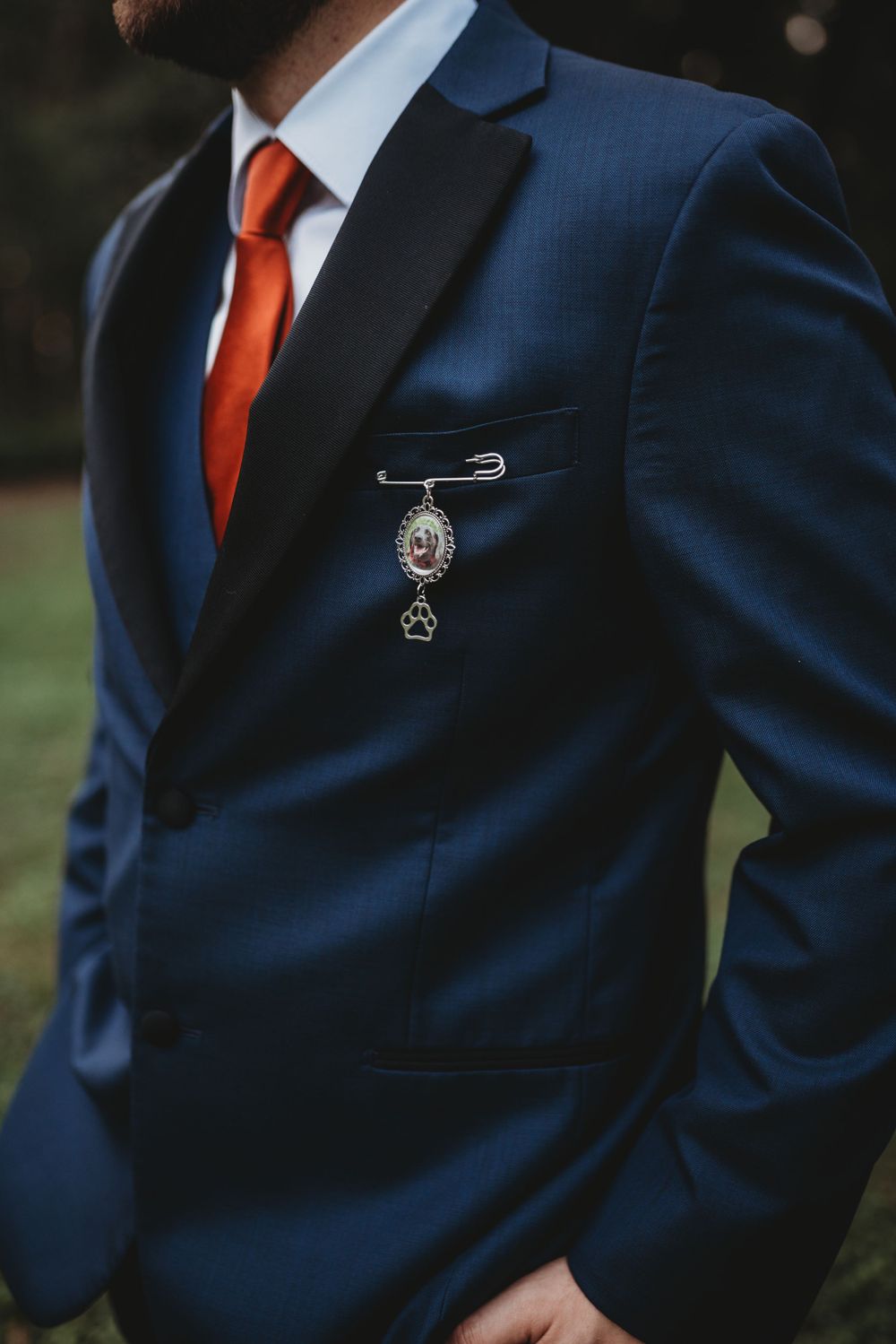 Close-up of navy blue suit jacket with red tie and decorative pin.