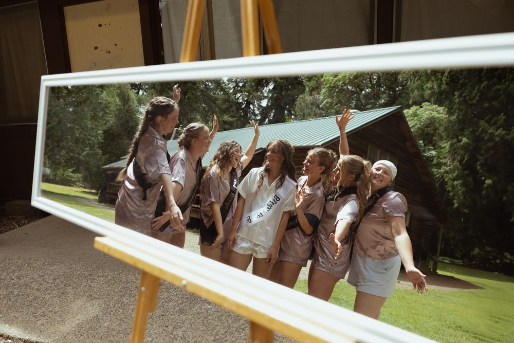 A framed panoramic photo of a group of girls posing and laughing outdoors at summer camp displayed on a wooden easel.